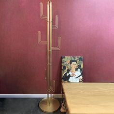 a tall metal cactus standing next to a table with a painting on the wall behind it