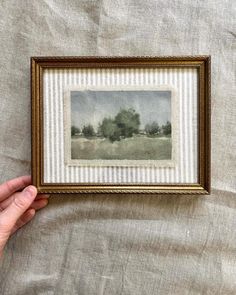 a person holding up a painting in front of a white sheet with stripes on it