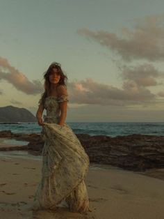 a woman standing on top of a sandy beach next to the ocean wearing a dress