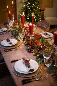 the table is set for christmas dinner with candles and greenery on each place setting