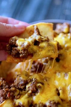 a hand holding a piece of cheesy bread with ground beef and cheese on it