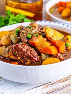 two white bowls filled with beef stew on top of a blue and white striped napkin