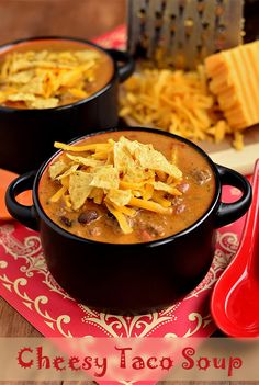 a black bowl filled with chili and cheese on top of a red place mat next to a spoon