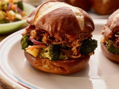 two pulled pork sandwiches with broccoli on a plate next to other food items