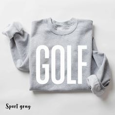 a gray sweatshirt with the word golf printed on it, sitting on a white surface