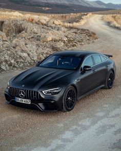 a black car parked on the side of a dirt road in front of some rocks