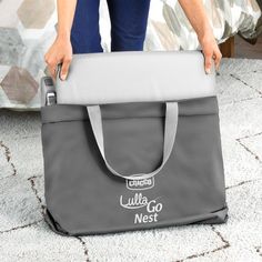 a woman holding onto a gray bag on top of a carpeted floor next to a bed