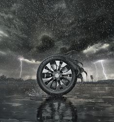 a black and white photo of a tire on the ground with lightning in the background