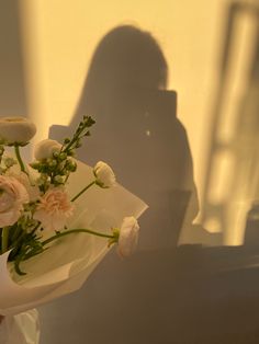 a woman holding a bouquet of white and pink flowers in front of her face with the shadow of a person behind her