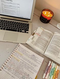 an open book sitting on top of a desk next to a laptop computer and notebook