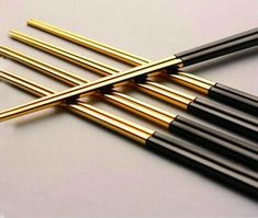 six black and gold colored straws on a white surface