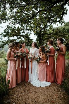 a group of women standing next to each other on top of a dirt road with trees in the background