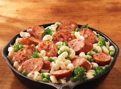 a skillet filled with pasta and sausages on top of a wooden table next to a fork