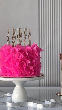 a cake with pink icing and gold candles on top is sitting on a table