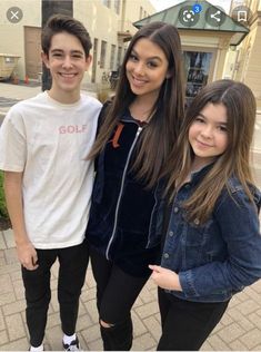 three young people standing next to each other in front of a brick sidewalk and building