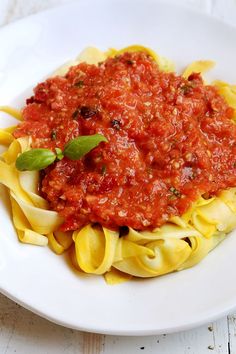 a white plate topped with pasta covered in marinara sauce and garnished with basil