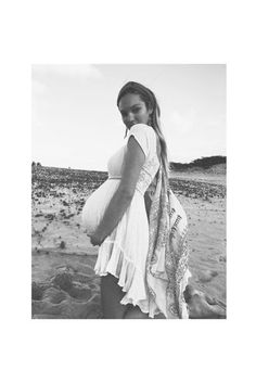 a pregnant woman is standing on the beach