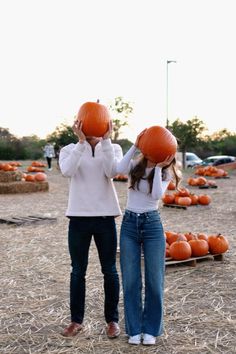 two girls with pumpkins on their heads standing in front of some hay bales