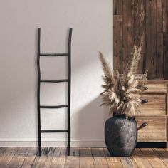 a tall wooden ladder leaning against a wall next to a vase with dry grass in it