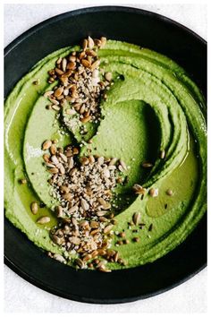 a bowl filled with green smoothie topped with nuts and seeds on top of it