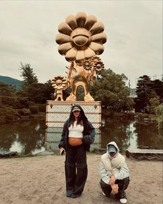 two people kneeling down in front of a large statue with a giant flower on it