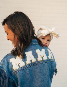 a woman holding a child wearing a denim jacket with the word mam on it