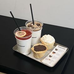 two cups of coffee and some pastries on a metal tray with black straws