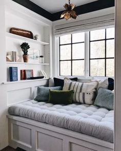 a window seat in the corner of a room with pillows on it and bookshelves