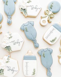 baby shower cookies are arranged on a white surface with greenery and blue onesuits