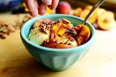 a person scooping ice cream out of a bowl with peaches and granola