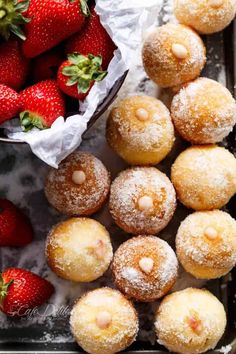 powdered sugar covered donuts and strawberries on a table