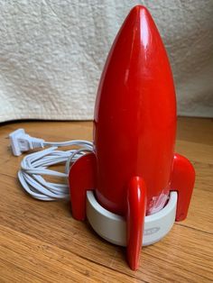 a red toy rocket sitting on top of a wooden table next to a charger