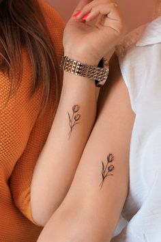 two women with matching tattoos on their arms, one is holding the other's arm