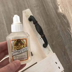 a hand holding a bottle of gorilla glue on top of a wooden table next to a knife