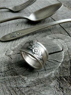 a silver ring sitting on top of a piece of wood next to two spoons