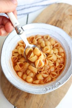 a person holding a spoon full of macaroni and cheese in a white bowl