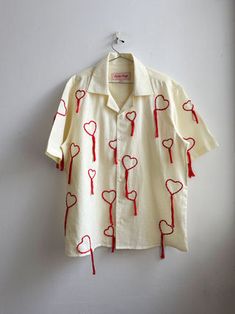 a white shirt with red hearts on it hanging from a hanger against a wall