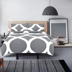 a bed with grey and white comforter in a room next to a lamp on a table