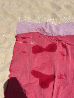 a red and white blanket laying on top of a sandy beach