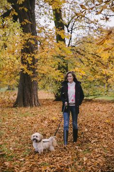 a woman is walking her dog through the leaves