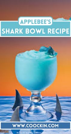 a blue drink sitting on top of a glass in the ocean with shark fin garnish