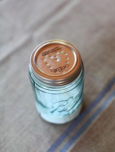 a blue mason jar sitting on top of a bed next to a striped table cloth