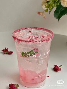 a pink drink in a plastic cup with ice and strawberries on the table next to flowers