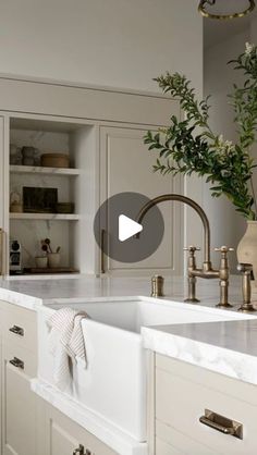 a kitchen with white cabinets and gold faucets, an open bookcase behind the sink