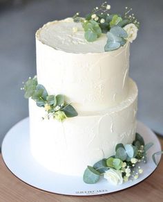 a three layer white cake with greenery on top