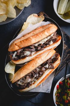 two large sandwiches sitting on top of a black plate next to chips and salads