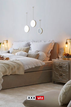 a bed with white sheets and pillows in a bedroom next to two lamps on the wall