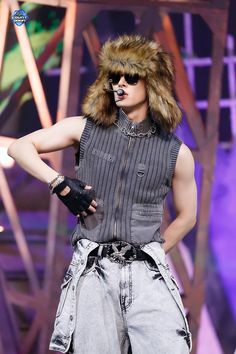 a man wearing a fur hat and sunglasses on stage with his hands in his pockets