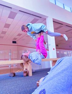 two people doing tricks on wooden benches in an indoor area with blue carpet and pink walls