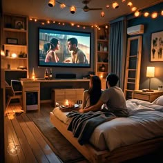 two people sitting on a bed in front of a flat screen tv with lights strung from the ceiling